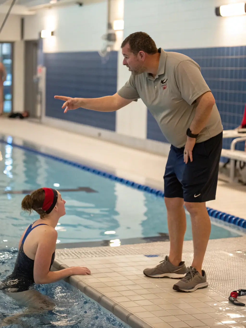 A coach providing one-on-one instruction to a young swimmer, focusing on stroke technique and improvement during a training session organized by COMITE DEPARTEMENTAL DE NATATION DE LA CHARENTE-MARITIME.