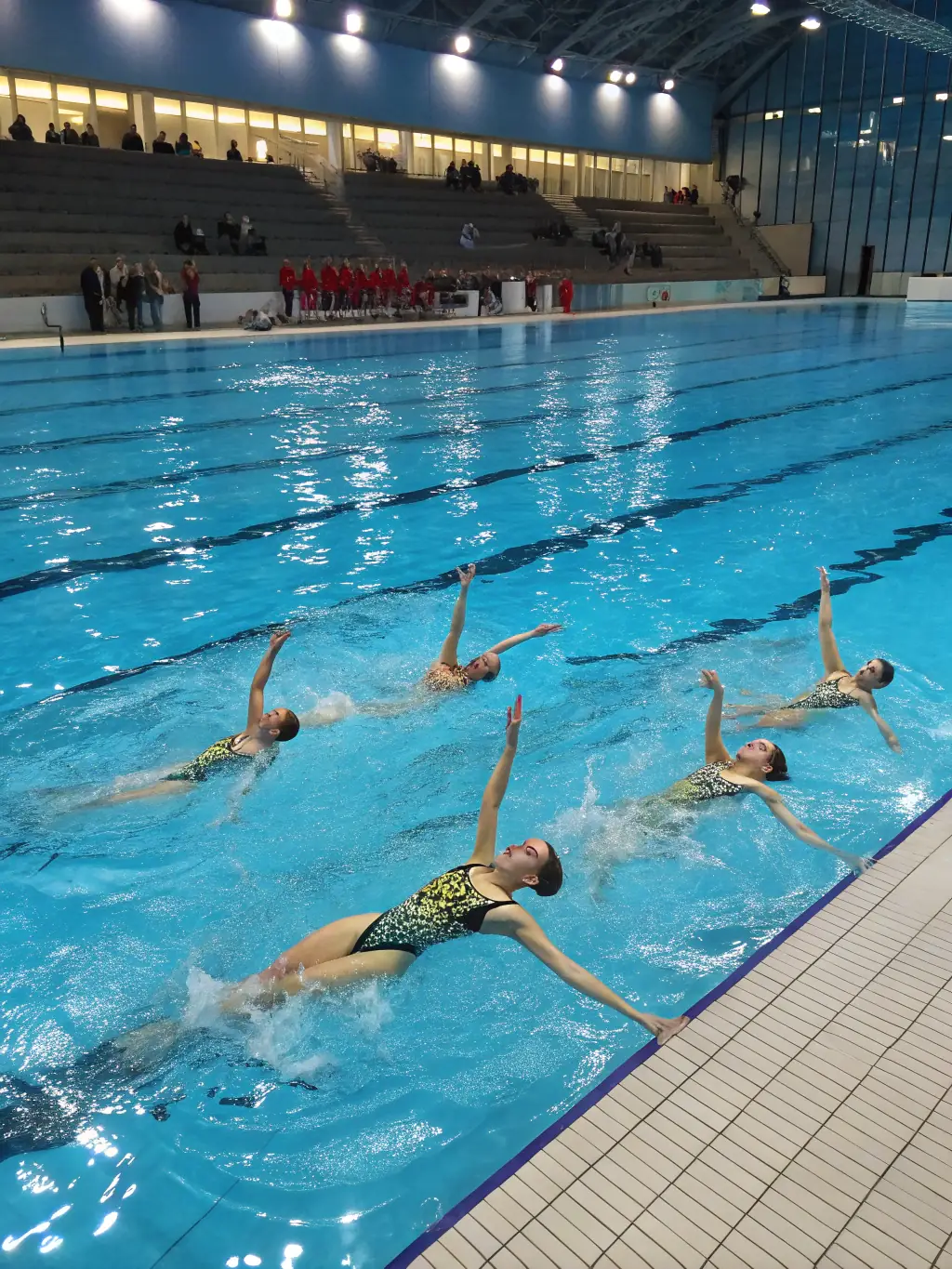A group of young swimmers practicing synchronized swimming in an indoor pool, focusing on teamwork and coordination.